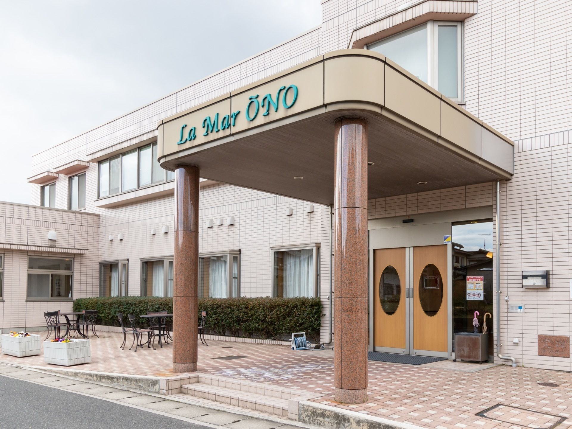 ２階建ての建物の玄関の様子である。玄関には小屋根があり、施設名が取り付けられている。また、玄関ドアは両開きの自動ドアである。