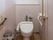 白を基調とした清潔感のあるトイレである。壁には手すりが取り付けられており、床にはふた付きの白色のゴミ箱が置かれている。