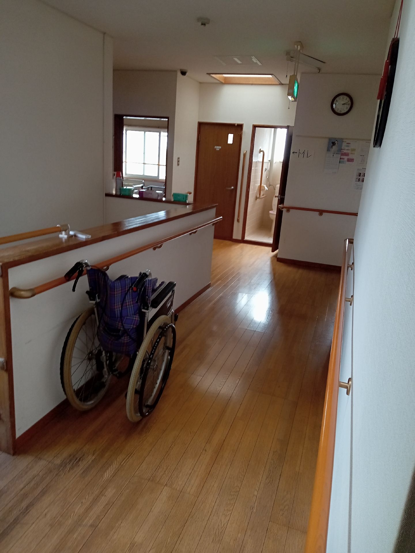 手すりが壁についている廊下の様子。車いすがたたんで一台置いてある様子