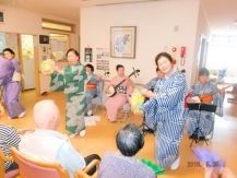 着物姿で踊りを踊る女性たちと三味線を弾く女性たちを、入居者が見ている。