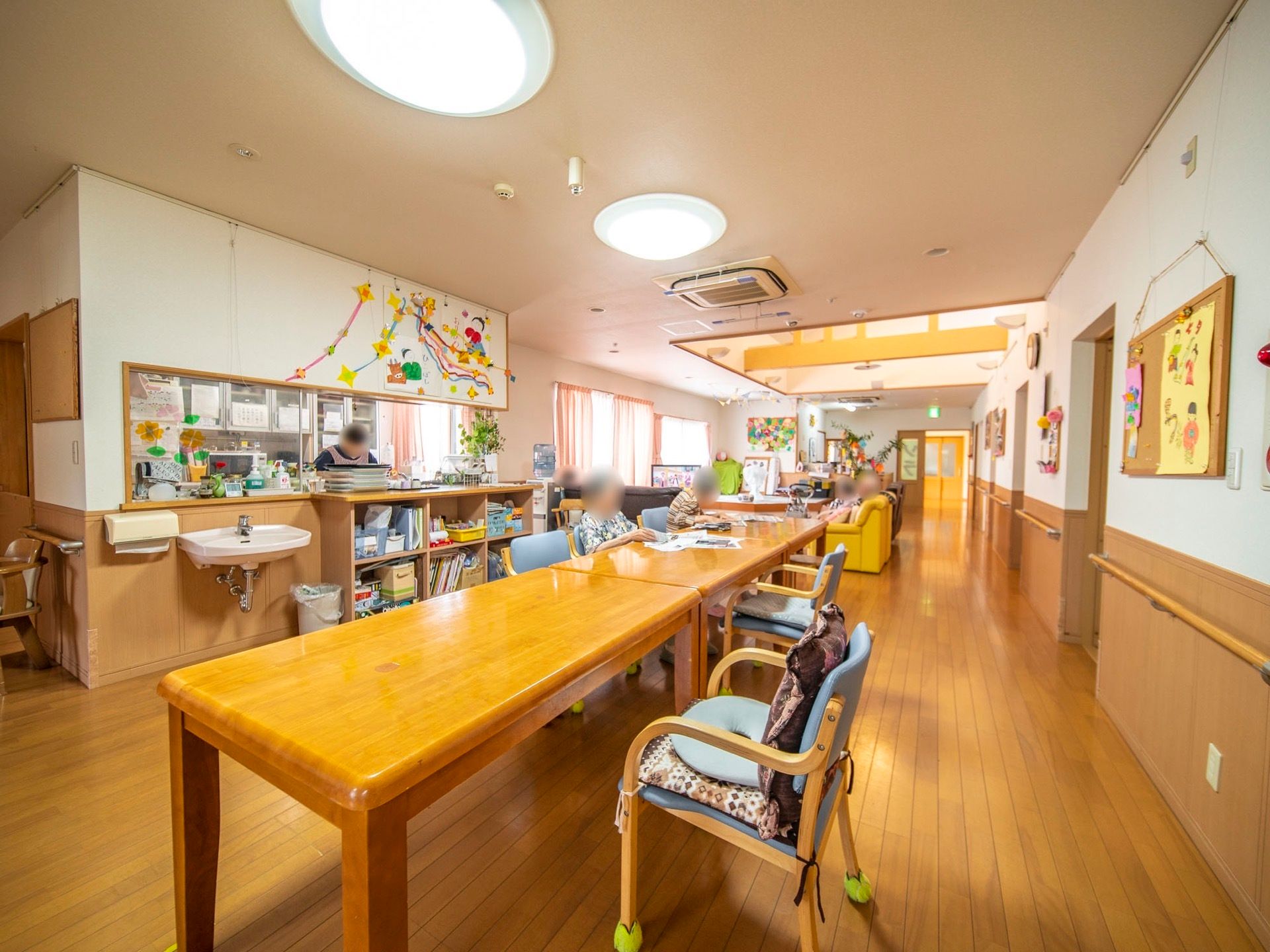 食堂に併設されたキッチンではスタッフが作業をしている。入居者様は雑誌を読んだりリビングでテレビ鑑賞をしたり、自由に過ごしている。
