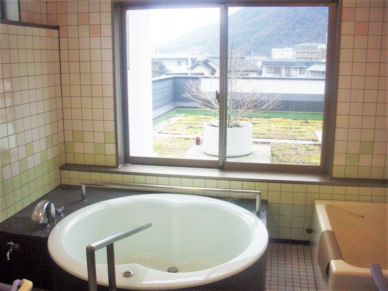 丸いジャグジー風の浴槽と窓の外に見える屋上を写した写真。施設内に設けられた浴室の様子