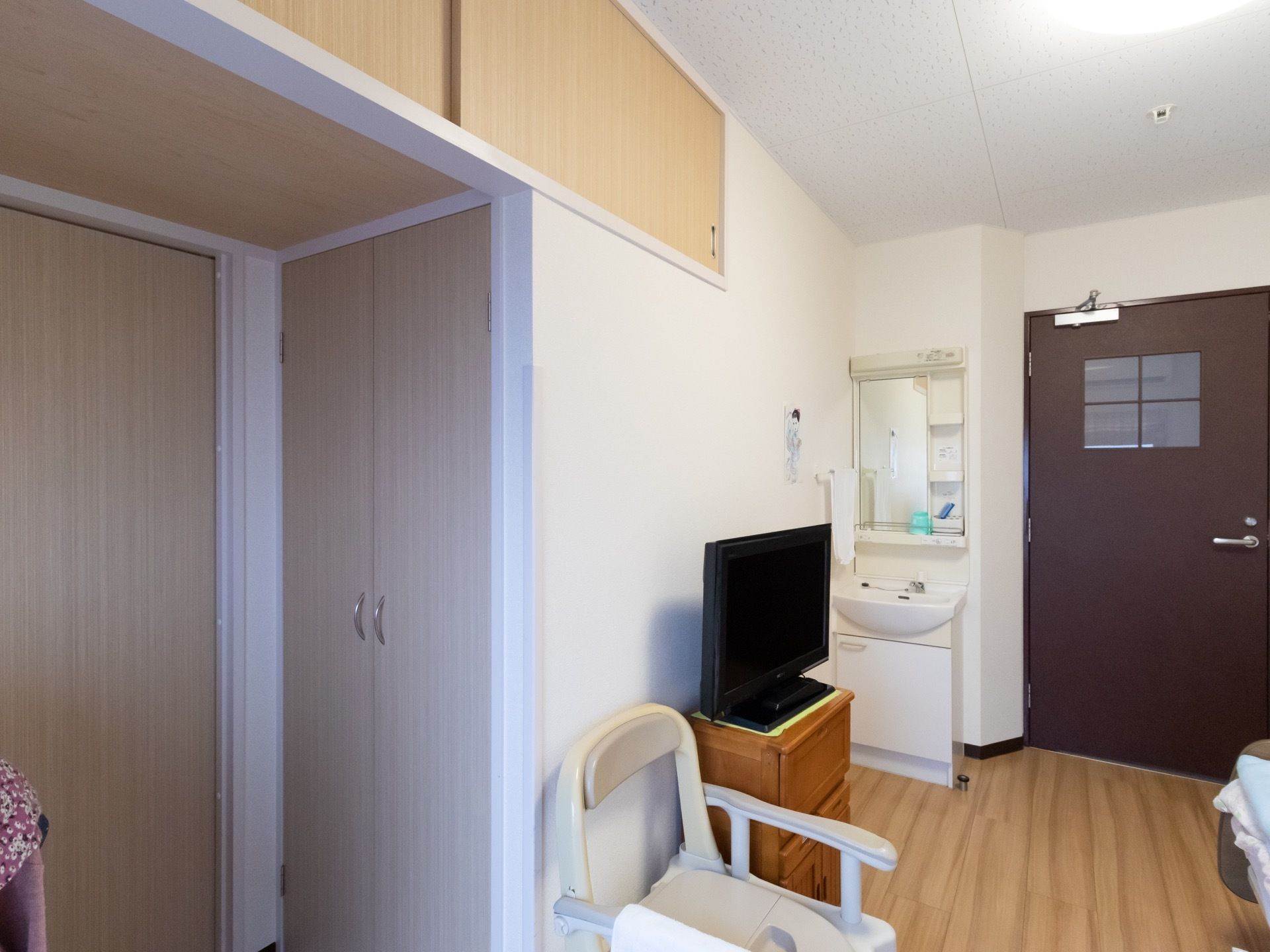 用意されている居室は壁が白く、清潔感がある。大きなクローゼットや洗面台、ベッド、椅子などが設置されている。