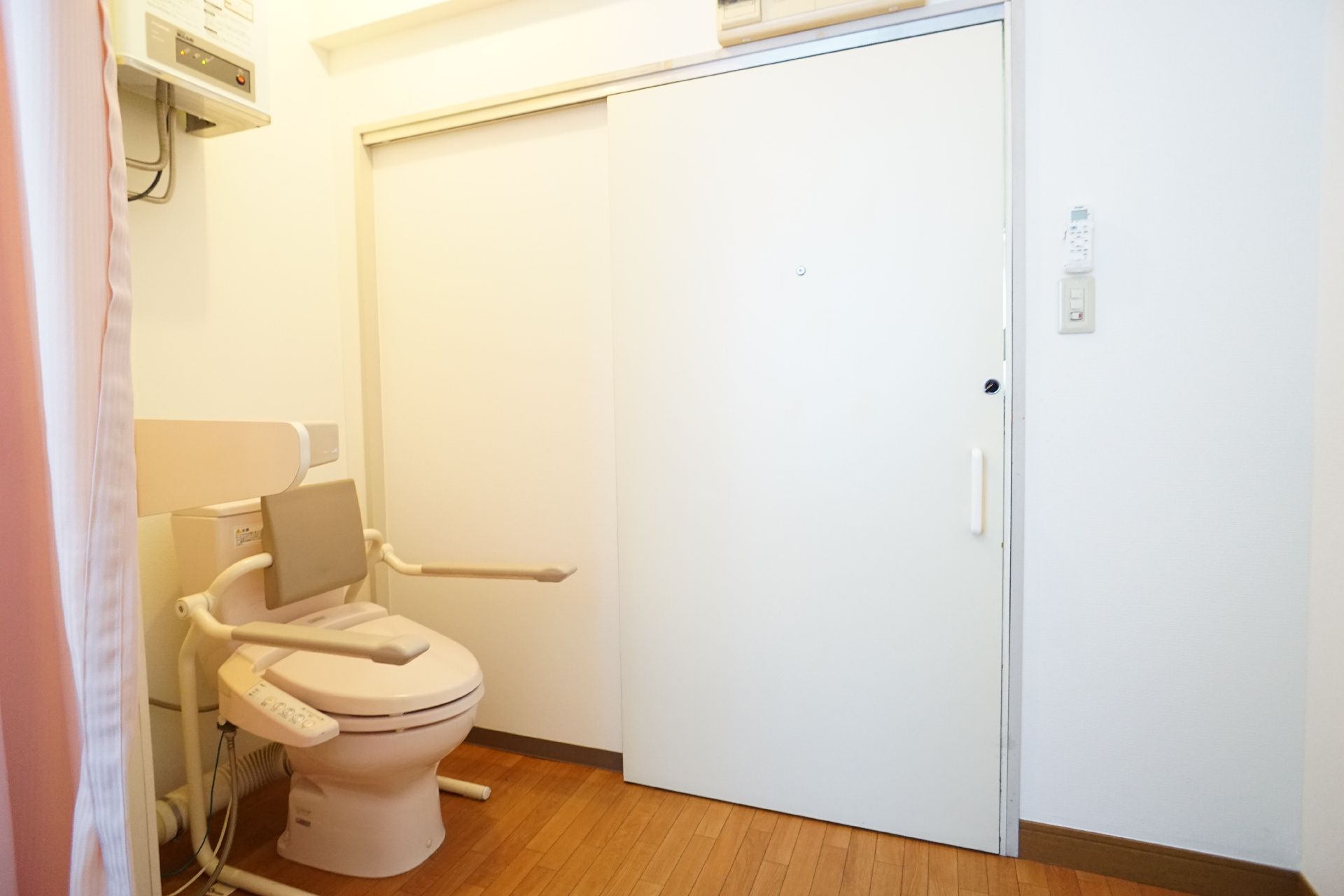 白い扉の前に配置された手すりに囲まれている洋式便器