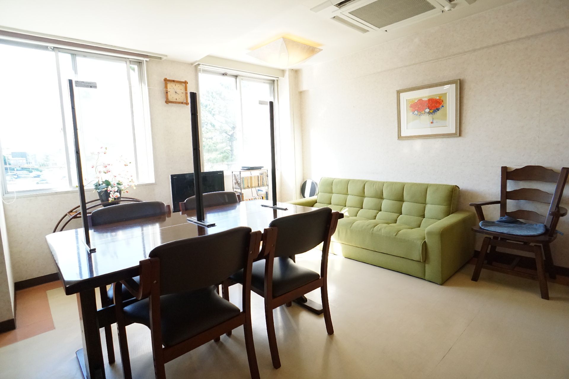 白い壁の部屋に置かれた緑のソファーと仕切りのついた木製の机