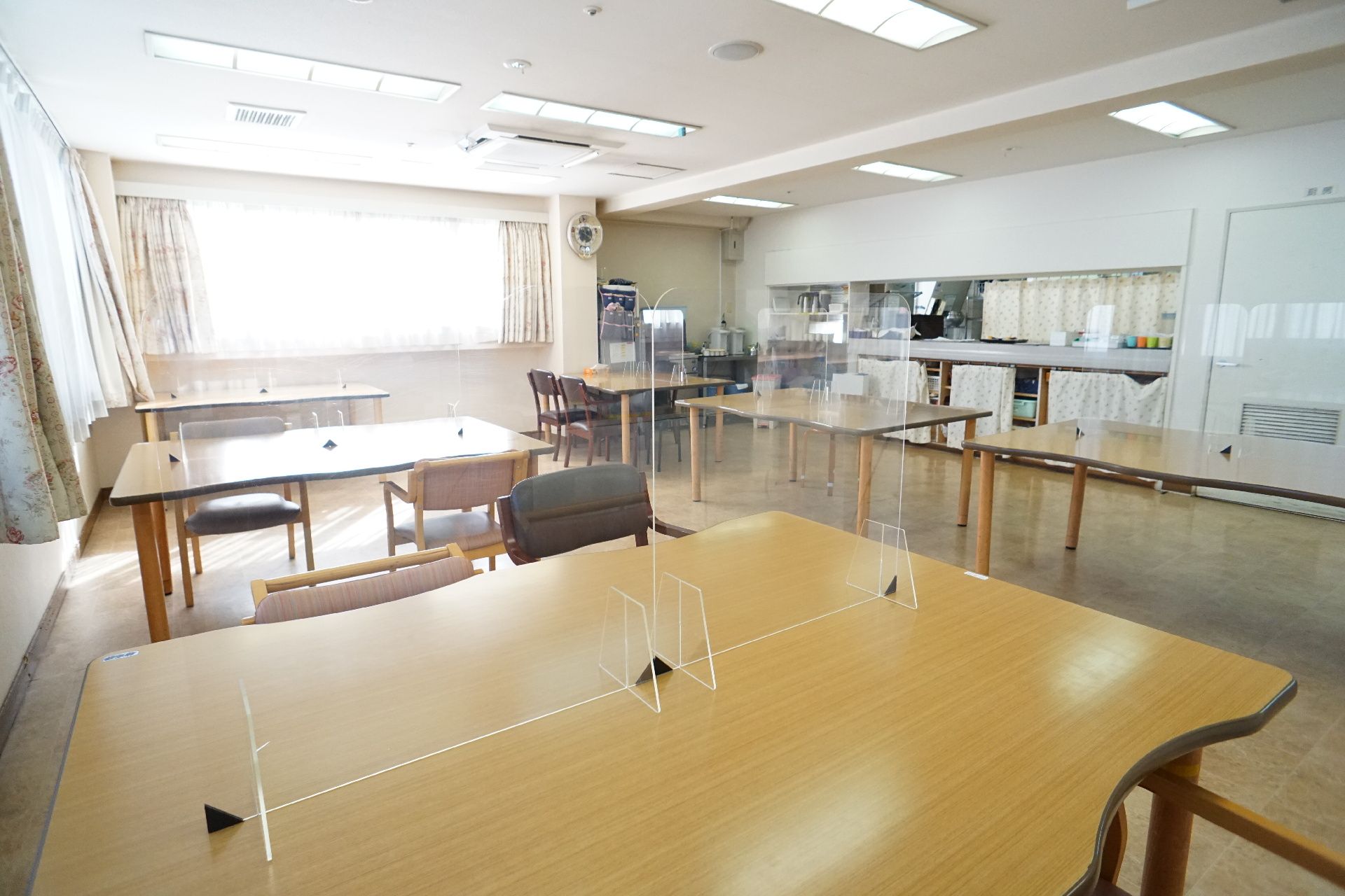 大きな窓がある白い壁の広間に置かれた透明な仕切りのついている木製の机