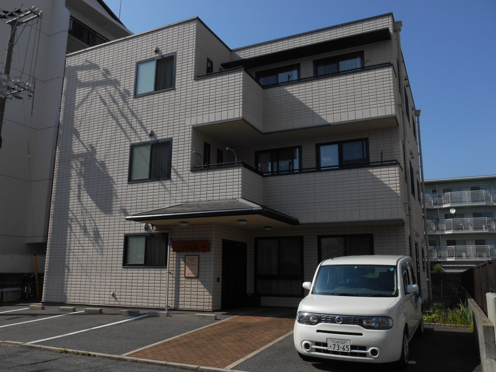 グレーでシックな外壁。駐車場には白い車が停まっている。