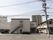 ベージュの壁の２階建ての建物がある。道路に面した角地に建っている。敷地内の一部が駐車場になっている。