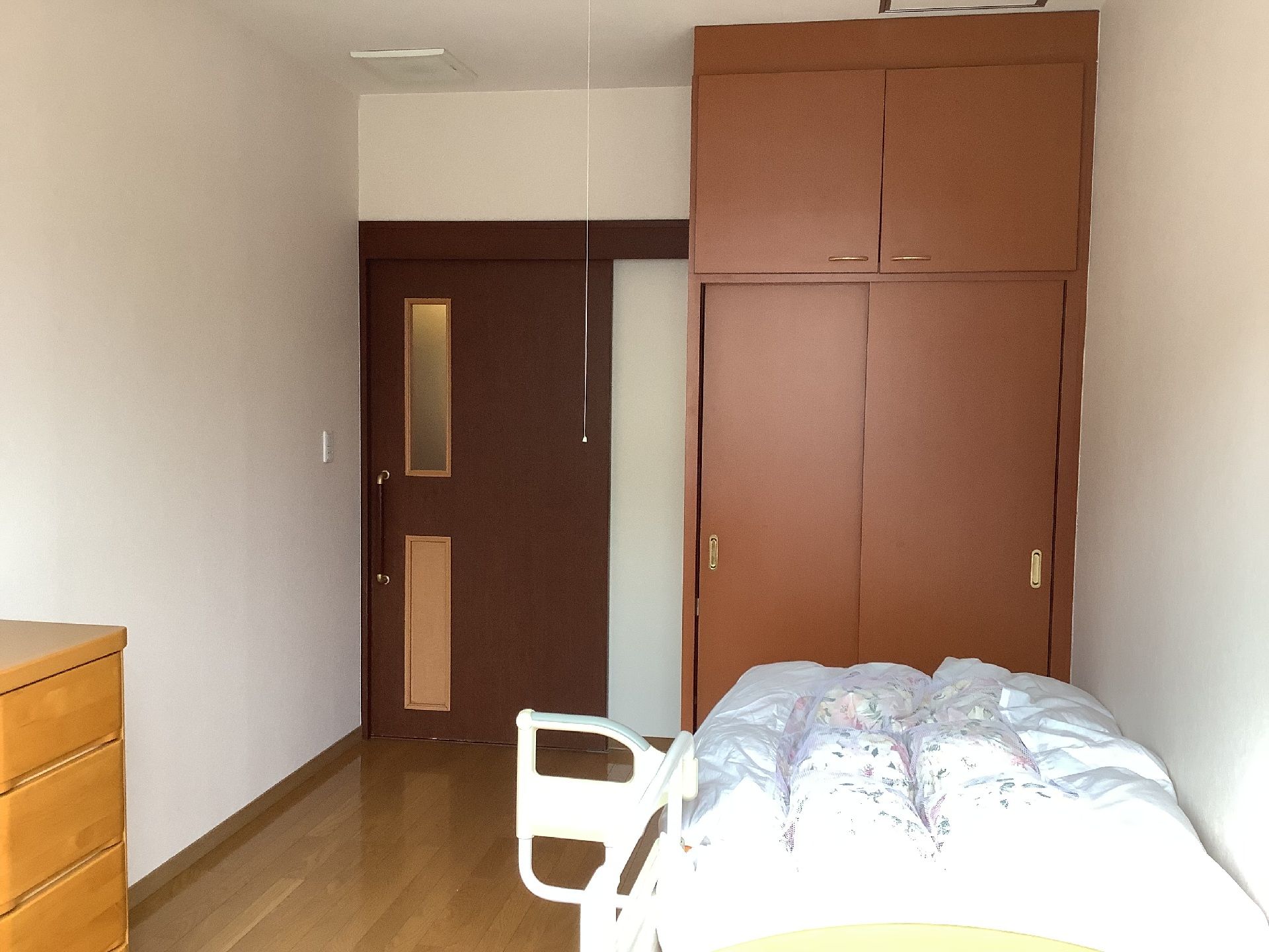 クローゼットが置かれ、タンスや寝具付きのベッドもあるフローリングの部屋。