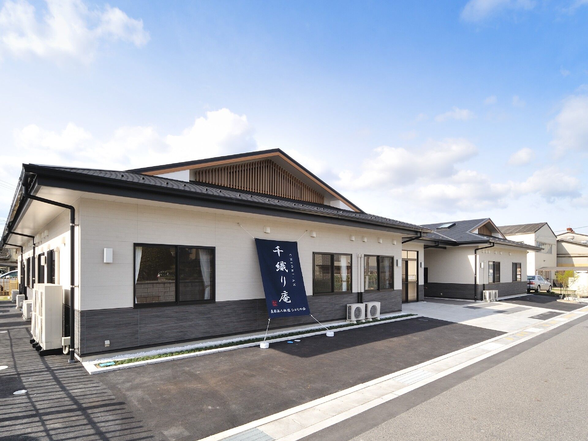 平屋建てで、グレーの瓦屋根が付いた平屋建ての建物の前には車を止める駐車場もある。