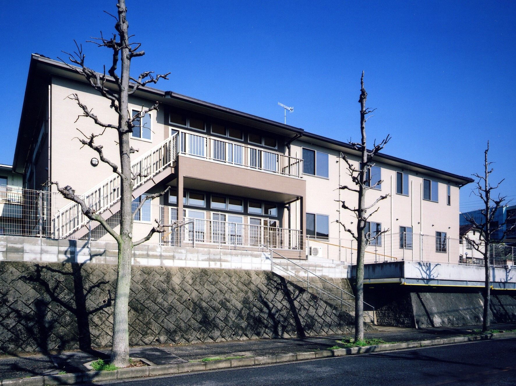 玄関に屋根が付いた2階建ての建物はベージュで、駐車場も完備されている。