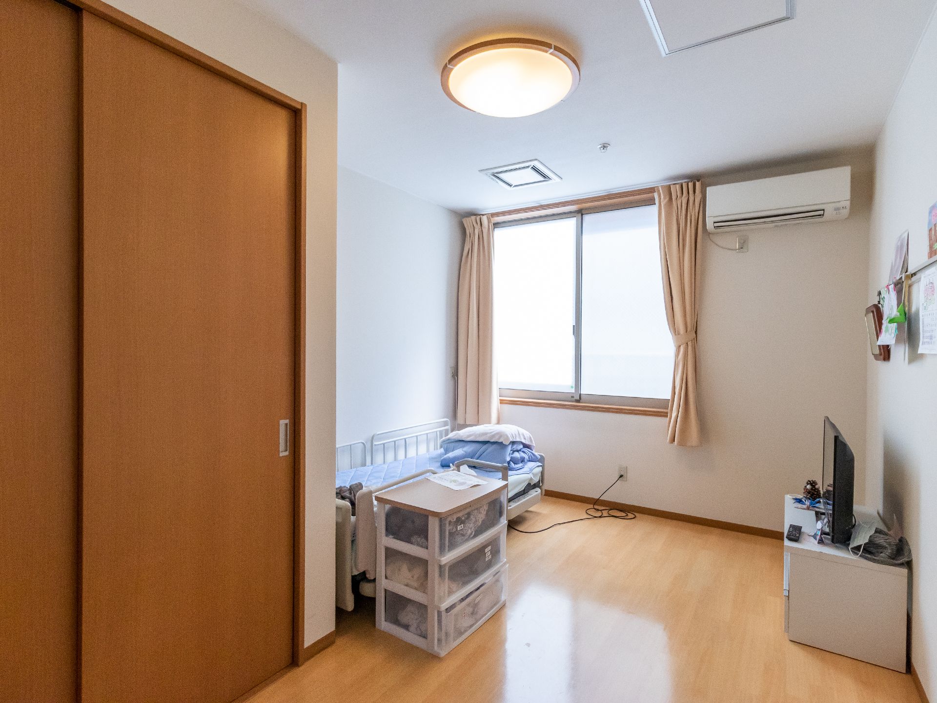大きな窓があり、介護ベット、収納などが置かれている居室