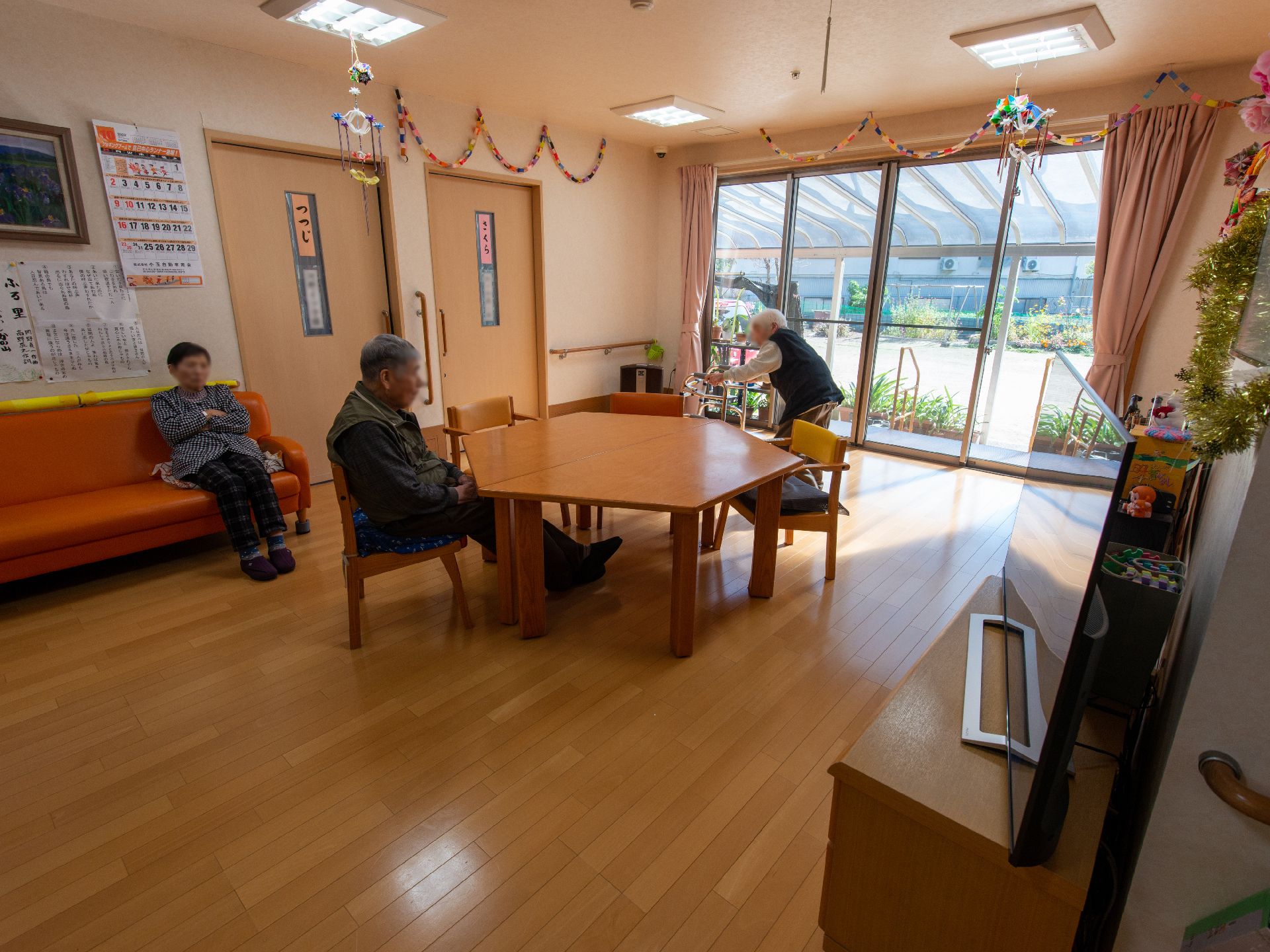 車いすの高齢女性と付き添いの高齢男性。屋外で男女のスタッフに囲まれて笑顔で過ごしている。