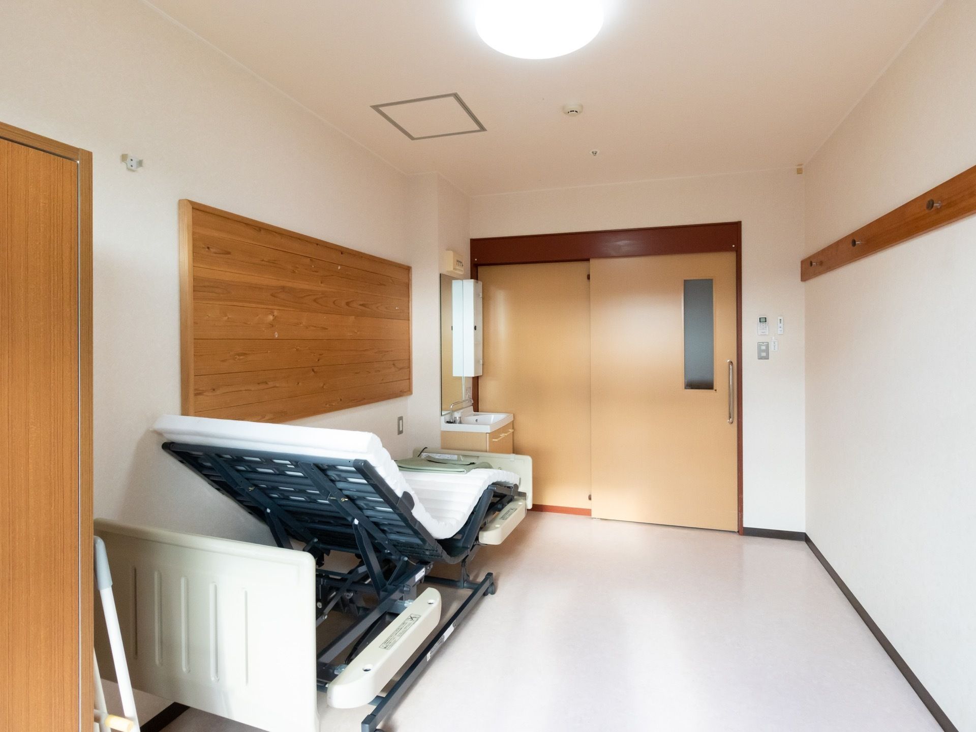 ご入居前の陽射しの入る居室である。洗面台と電動ベッドが設置され、壁には木製のボードが配備されている。