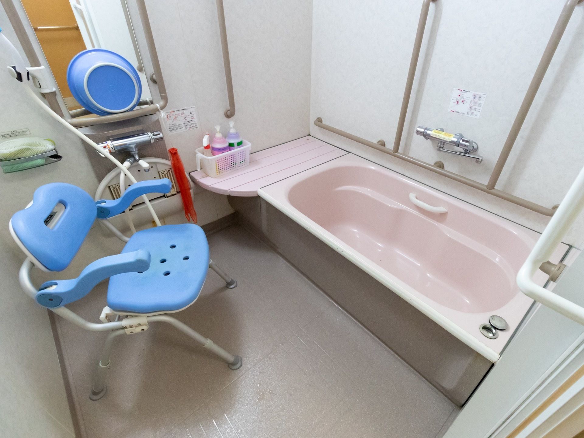 浴室には、浴槽の中がピンク系のユニットバスが設置され、ブルー系のバスチェアーが洗い場に置かれている。