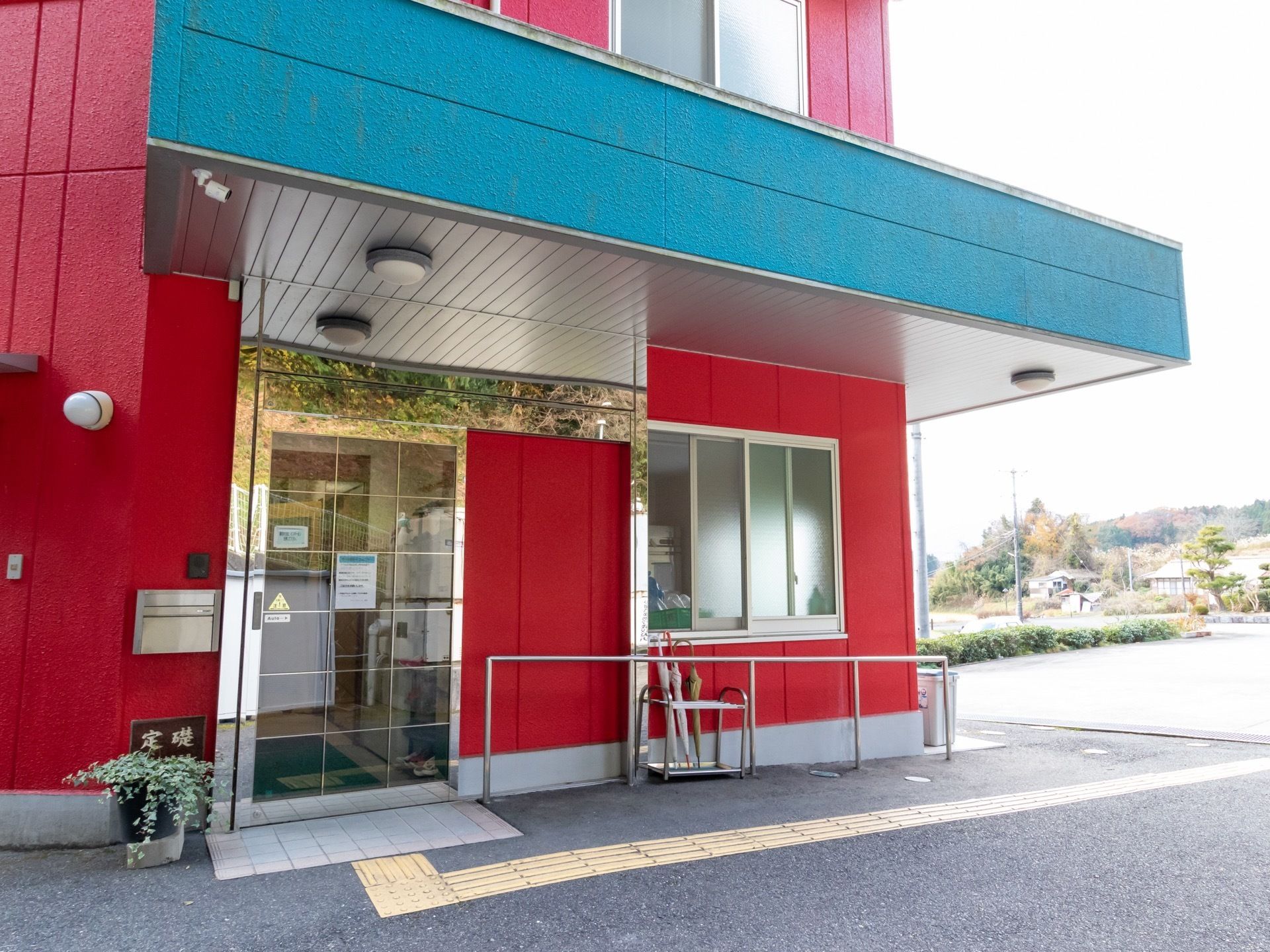 インパクトあるレッド系とブルー系の外壁に施設入口が設けられている。手すりや点字ブロックが設置されている。