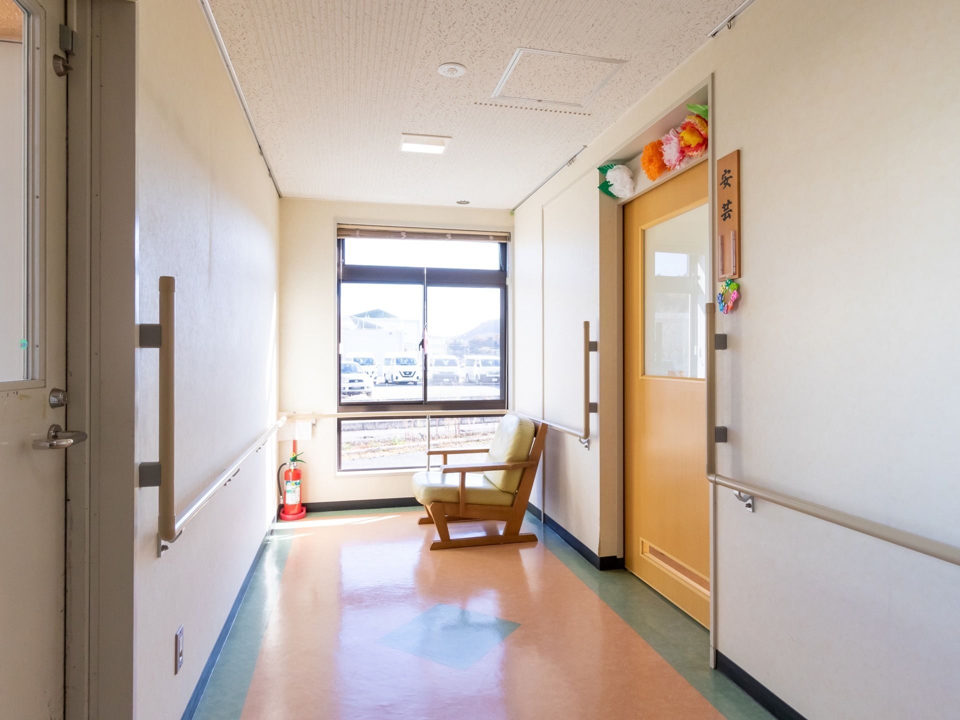 通路の行き止まりに窓があり、ひじ掛け付きの椅子が置かれている。壁や窓には手すりがある。