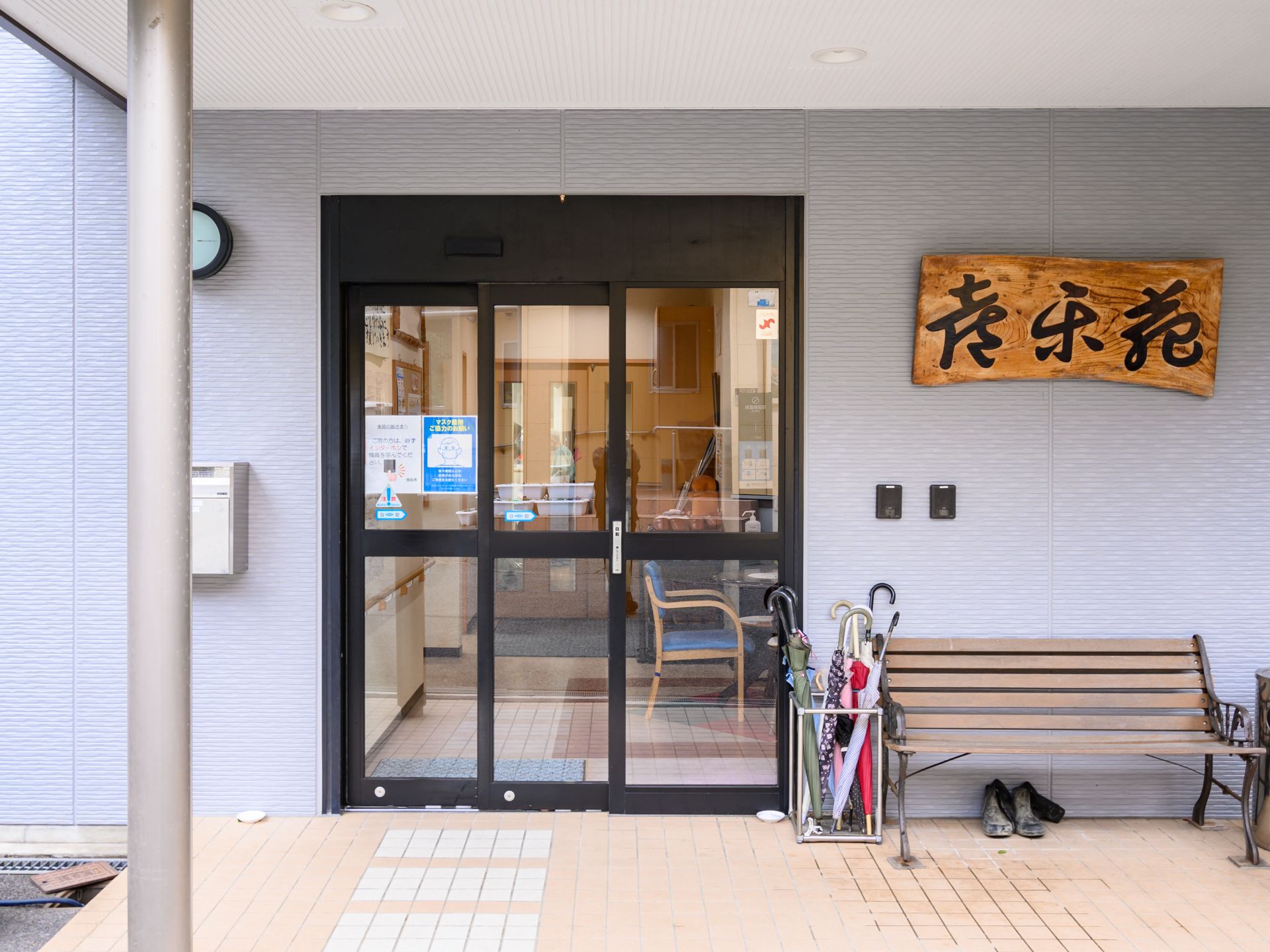 車いすの高齢女性と付き添いの高齢男性が若い男女のスタッフに囲まれ、笑顔で屋外で過ごしている。
