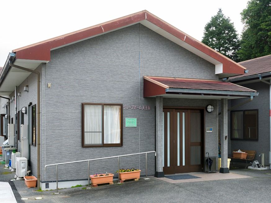 手すりが付いた玄関。グレーの外壁の平屋建ての建物は家庭的な雰囲気。