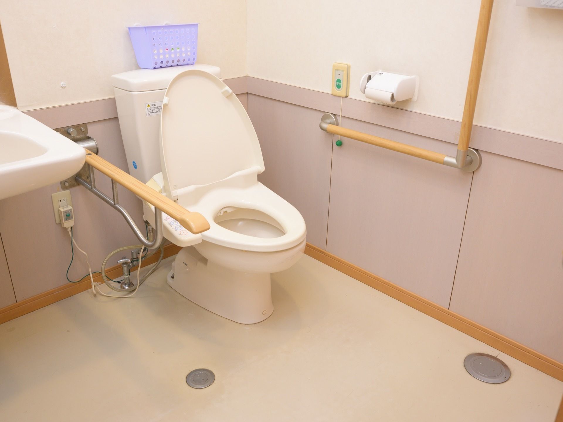 清潔感のあるトイレである。壁にはＬ字型の手すりやナースコール、ペーパーホルダーがかかっている。