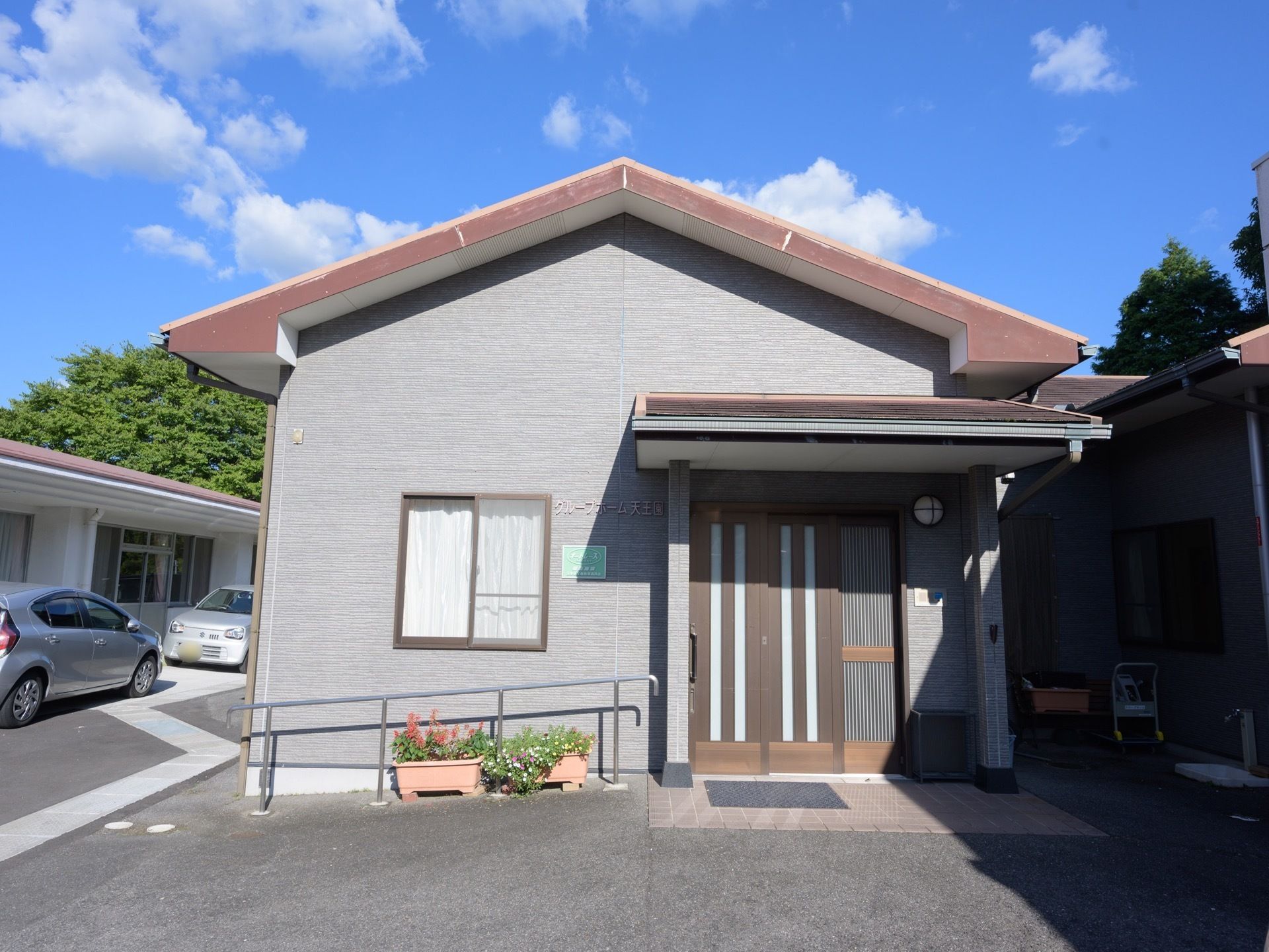 １階建てのグループホームで、玄関横には手すりがある。入口はスライド式となっており、下にはマットがある。