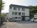 施設は3階建てで、白い外壁に黒い三角屋根の造りとなっている。施設敷地内に駐車スペースがあり、車が数台止められている。