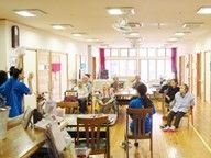 共有スペースでレクリエーションを楽しむ入居者とスタッフ。窓がたくさんあり明るい空間。