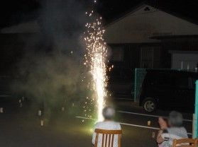 噴射式の花火が勢いよく上がっている様子。いすに座ってみている入居者の後ろ姿が見える。