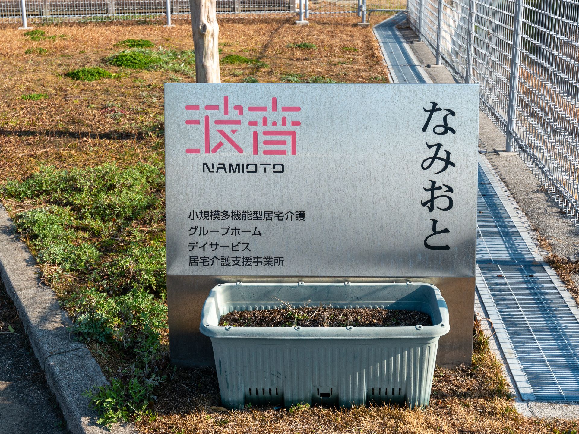 日当たりのいい室内で笑顔で話しているピンクのエプロンを付けた若い女性スタッフと車いすの高齢女性。