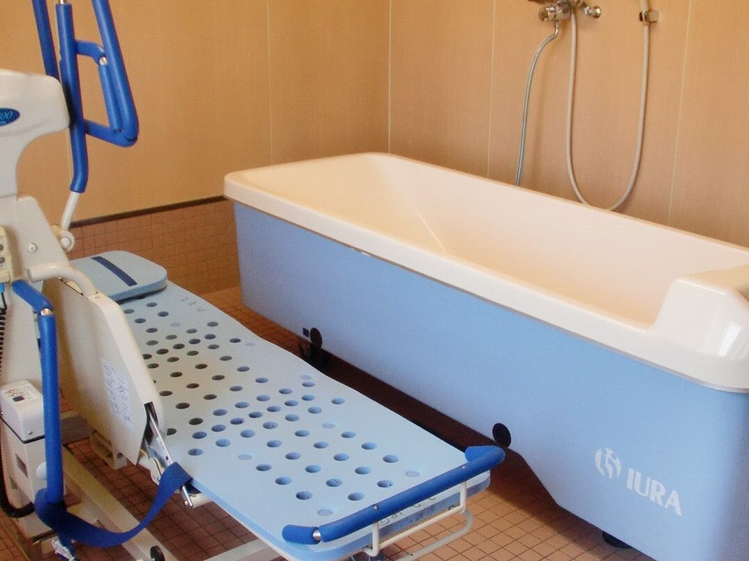 白と青の機械浴が設置されたベージュの浴室にはシャワーも付いている。寝たまま入浴できる機械浴。
