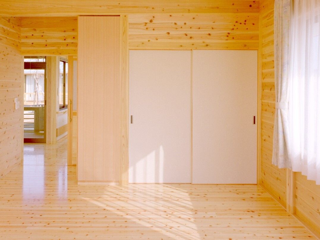 カーテンがついた大きな窓がついたフローリングの部屋には大型の収納家具が付き、ドアの外には共有スペースが見える。
