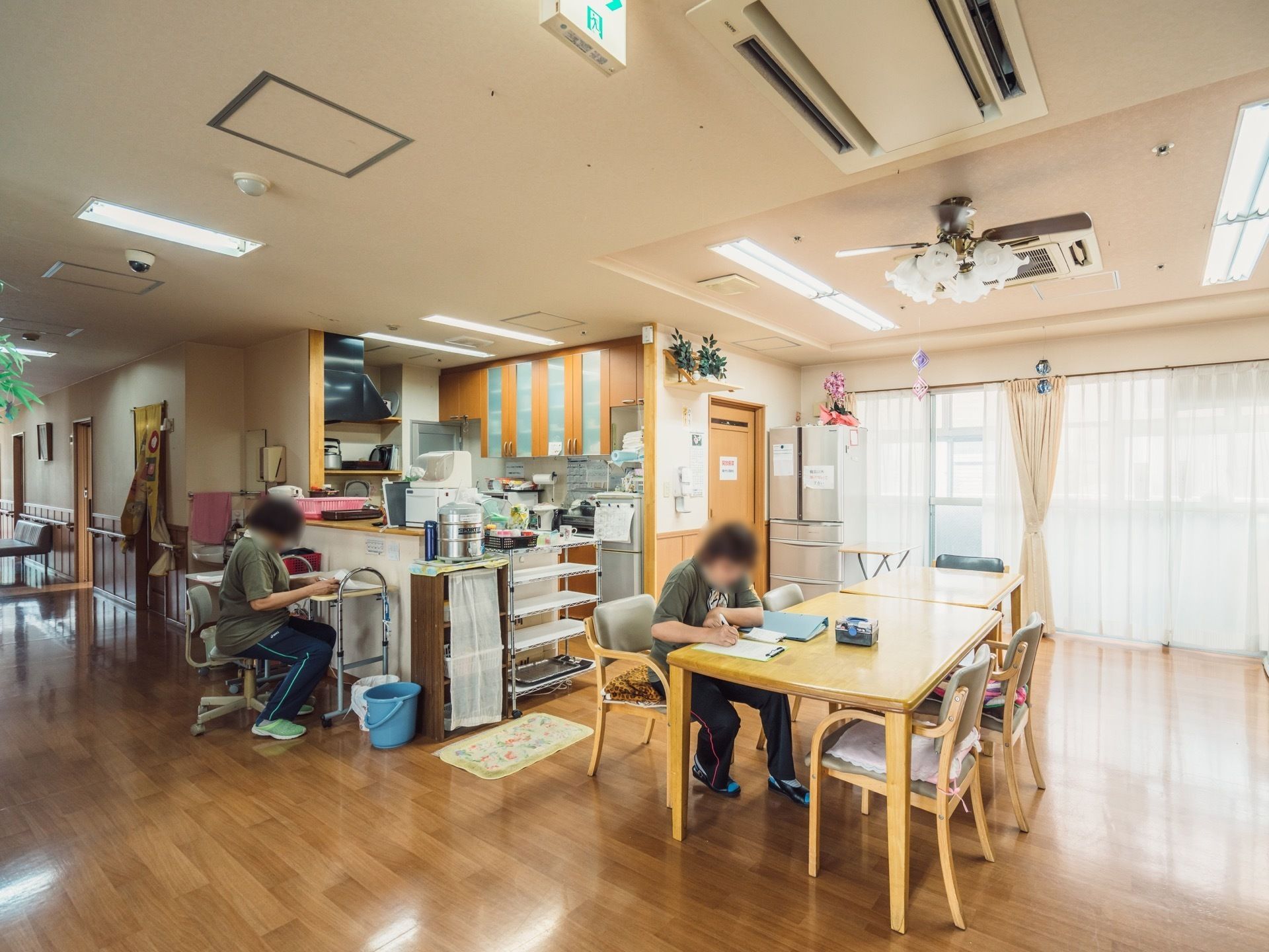 食堂では２名のスタッフが冊子への記載業務をしている。台所が併設されており、スタッフと顔を合わせながら調理や食事をお楽しみいただける。