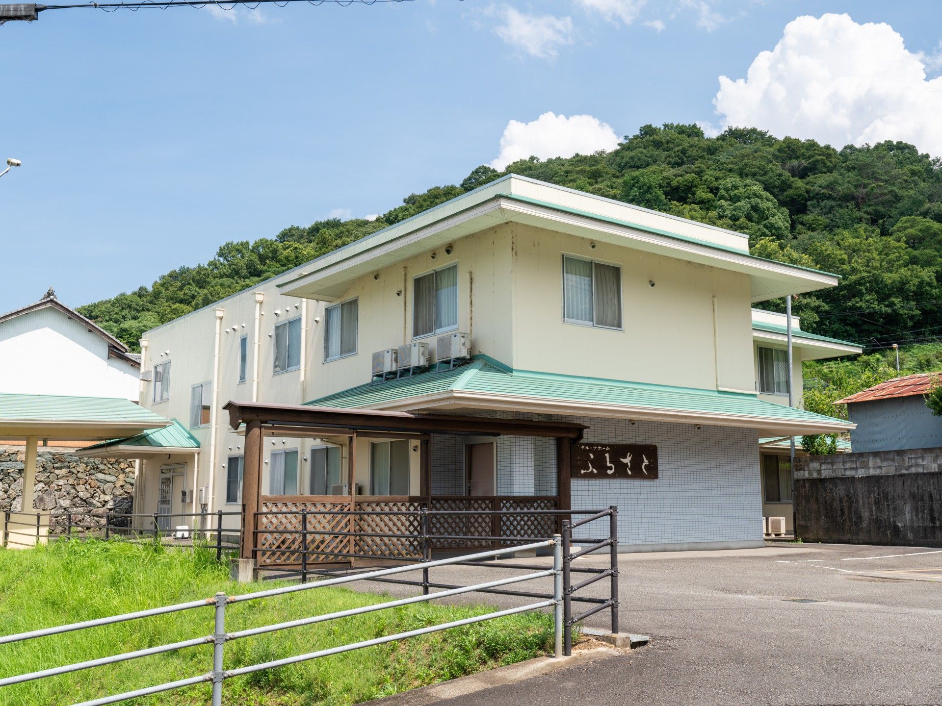 共有スペースのダイニングテーブルを囲んでいる入居者にお屠蘇をふるまって回っている黒いスーツ姿の男性スタッフ。高齢男性が杯を持って注いでもらっている。