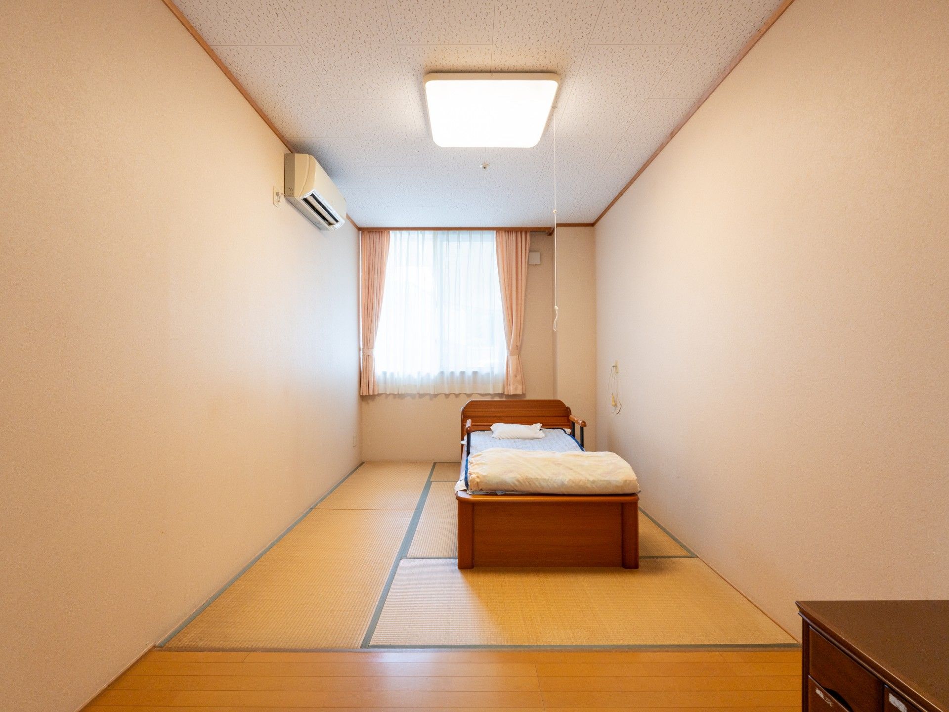 髪を後ろに束ねた若い女性スタッフが黒いにニット帽をかぶった高齢女性を抱きかかえる様にして介助している様子。