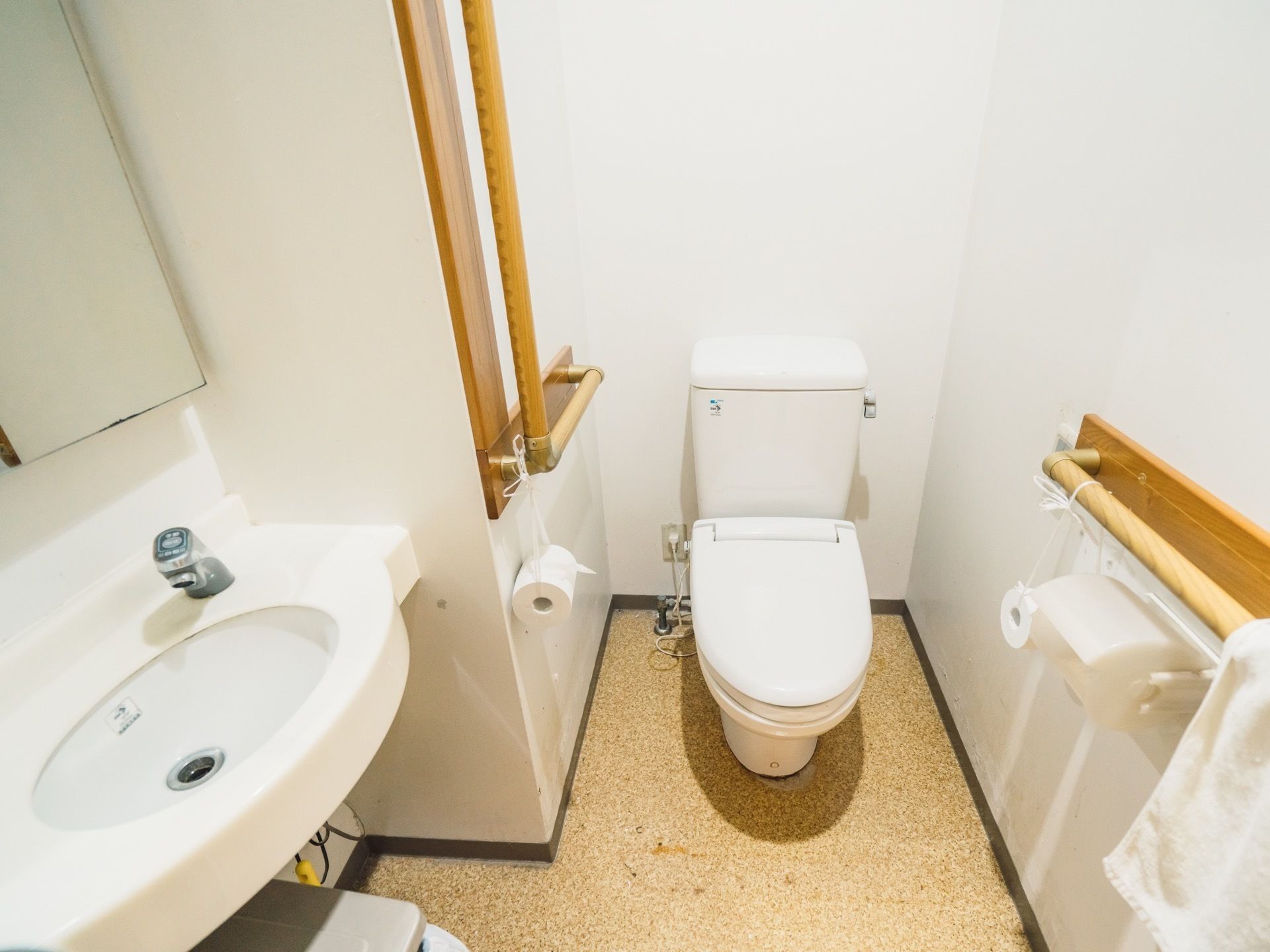 トイレの壁には、L型と水平型の手すりが設置されている。自動水栓付き洗面台が完備されており、ゴミ箱が置かれている。
