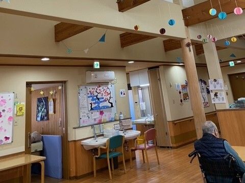 笑顔で屋外で過ごしている車いすの高齢女性と付き添いの高齢男性、若い男女のスタッフ。