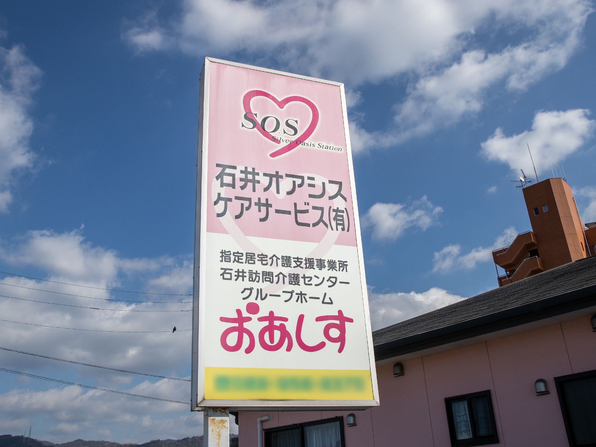 晴れた日に施設敷地内に立てかけられている看板である。施設名称と施設種別がロゴマークとともに明記されている。