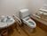 白い壁に薄茶色の床の広々としたトイレ。便座の両脇に手すりが設置されており、トイレの近くに洗面台も用意されている。