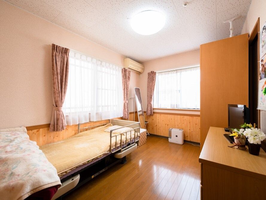 大きなタンスやテレビ、寝具付きのベッドが置かれたフローリングの部屋にはカーテンが付いた大きな窓が二つある。