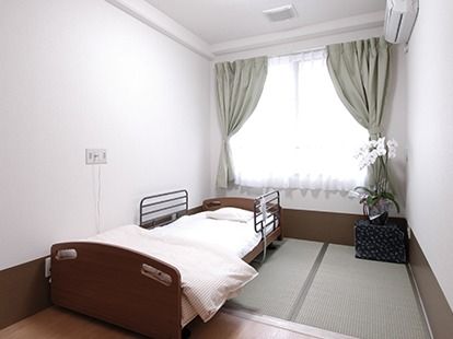 畳敷きのスペースがあるフローリングの部屋にはベッドが置かれ、大きな窓にはグレーのカーテンが付けられている。