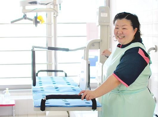 ストレッチャー浴の横で介助に当たろうとする女性スタッフ。満面の笑顔。