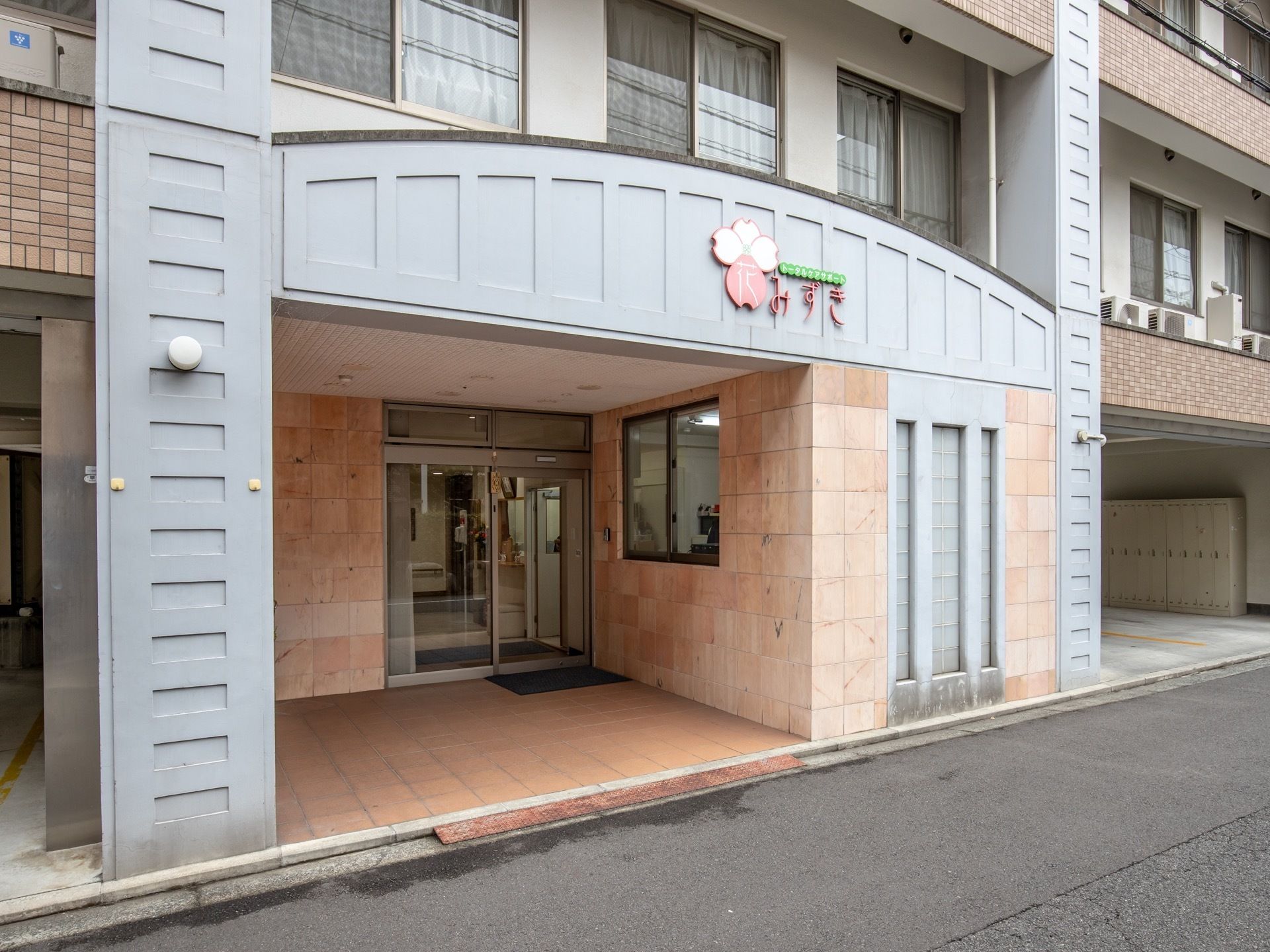 屋根付きの玄関でガラス張りの自動ドアとなっており、床にはマットが敷かれている。入口横にはスタッフルームが見える。