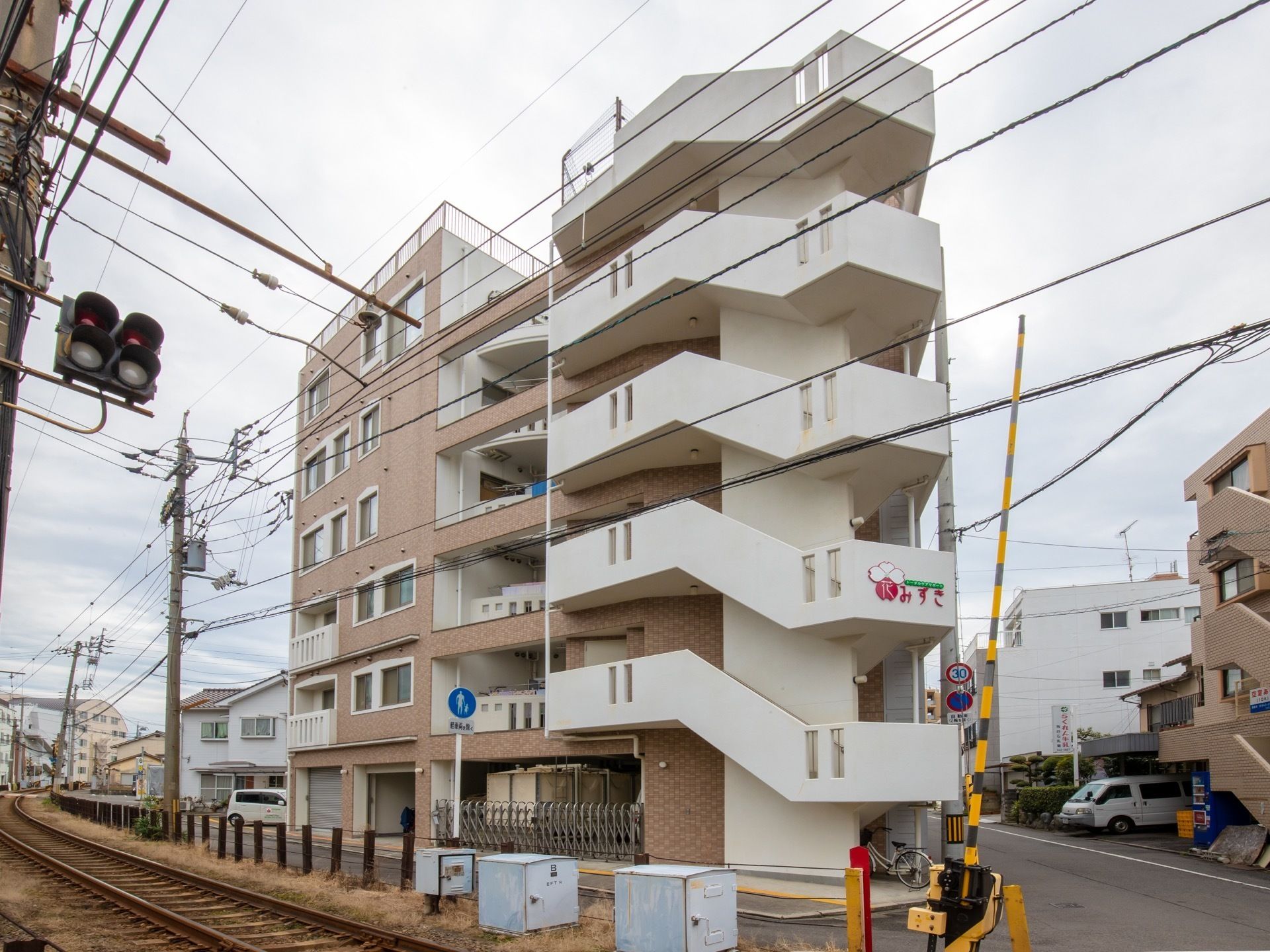 白を基調とした６階建ての大きなマンションのような外観のグループホームです。屋上部分には、転落防止のためフェンスが設置されている。