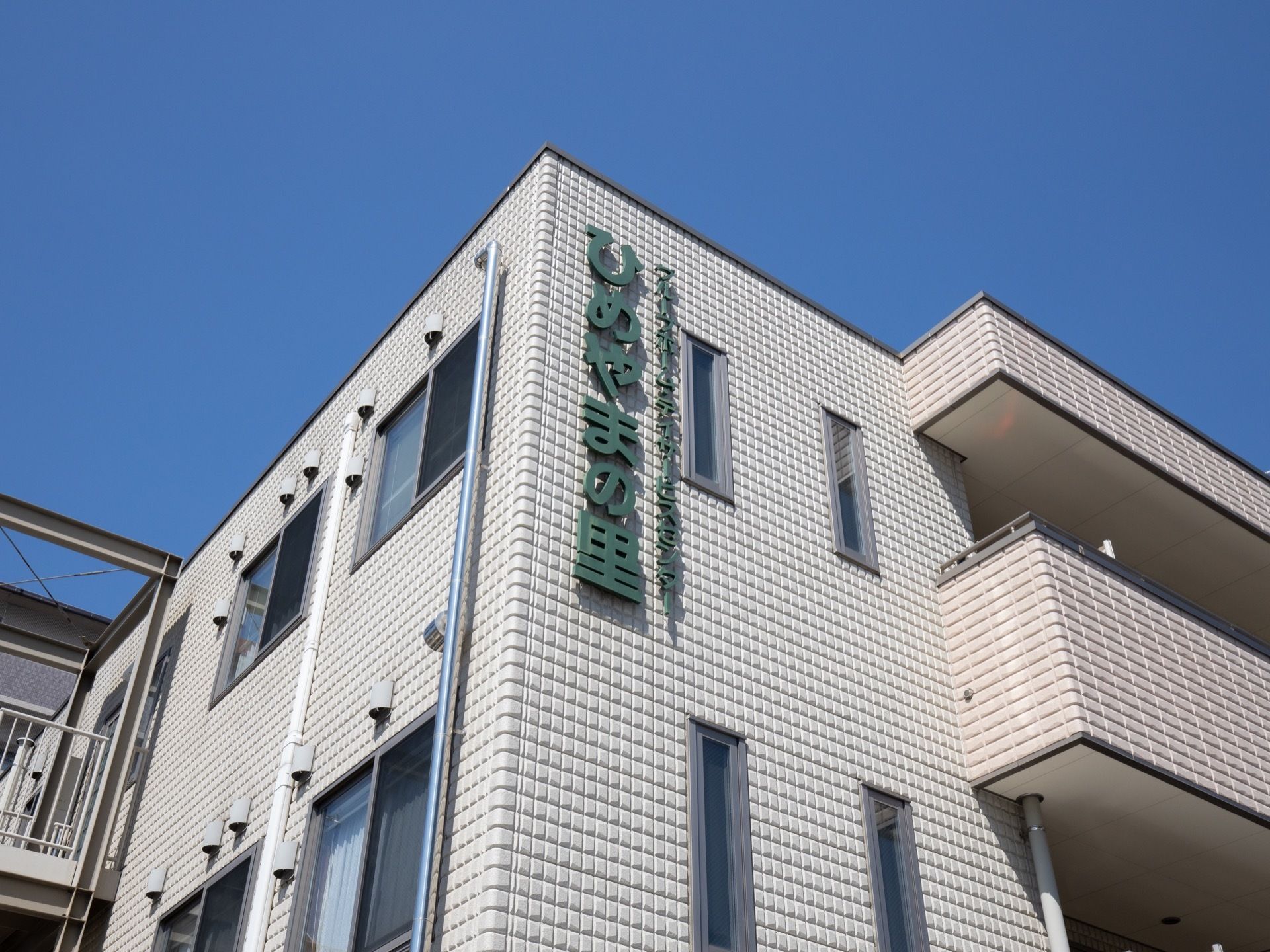 施設は白いタイル張りの３階建ての建物である。外壁には、大きく施設名が記されている。ベランダが設けられている。
