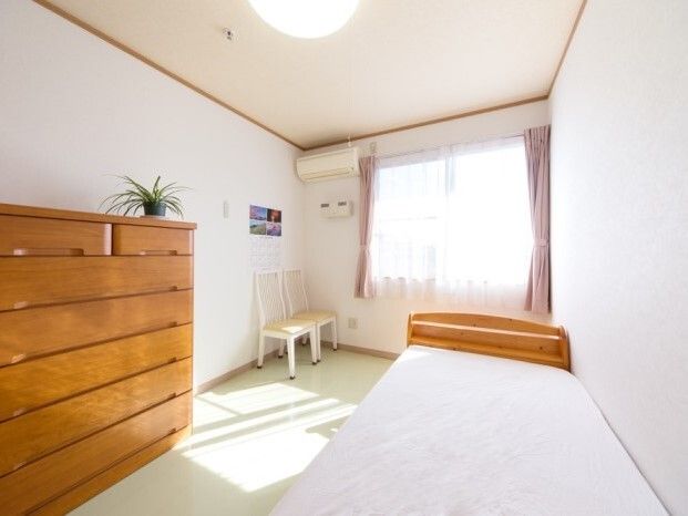 窓がある明るい部屋の様子。ベッドやタンスが置かれている小さなワンルームタイプ
