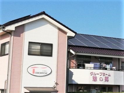 瓦屋根の建物の外観写真。グループホーム憩の郷の看板が付いている建物