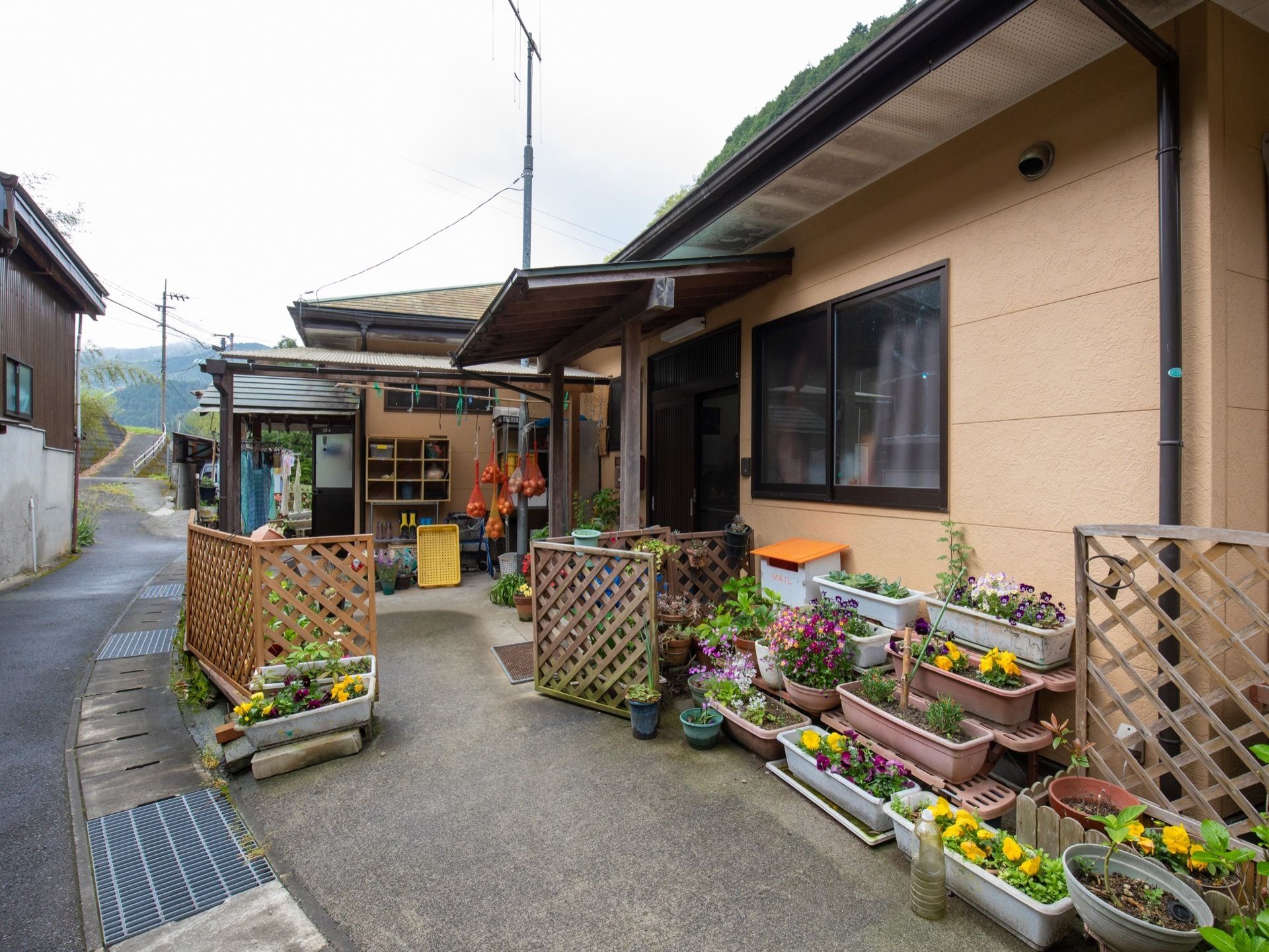 あたたかい色合いの外壁である。玄関の出入り口に屋根が設置されている。敷地には色とりどりの花が飾られている。