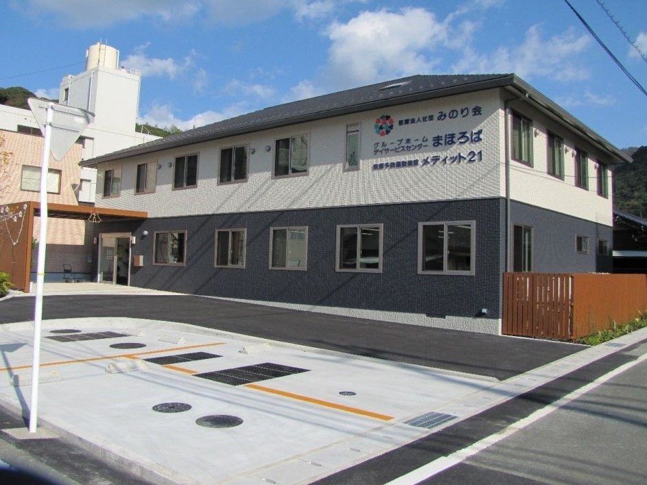 ２階建ての建物。玄関には屋根が付き、屋外には木製のフェンスがある。