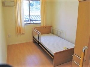 エアコンが付いたフローリングの居室。窓が大きくベッドもある。