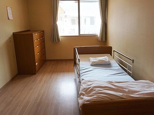 フローリングの部屋には寝具付きのベッドが置かれ、タンスが設置され、大きな窓が付いている。